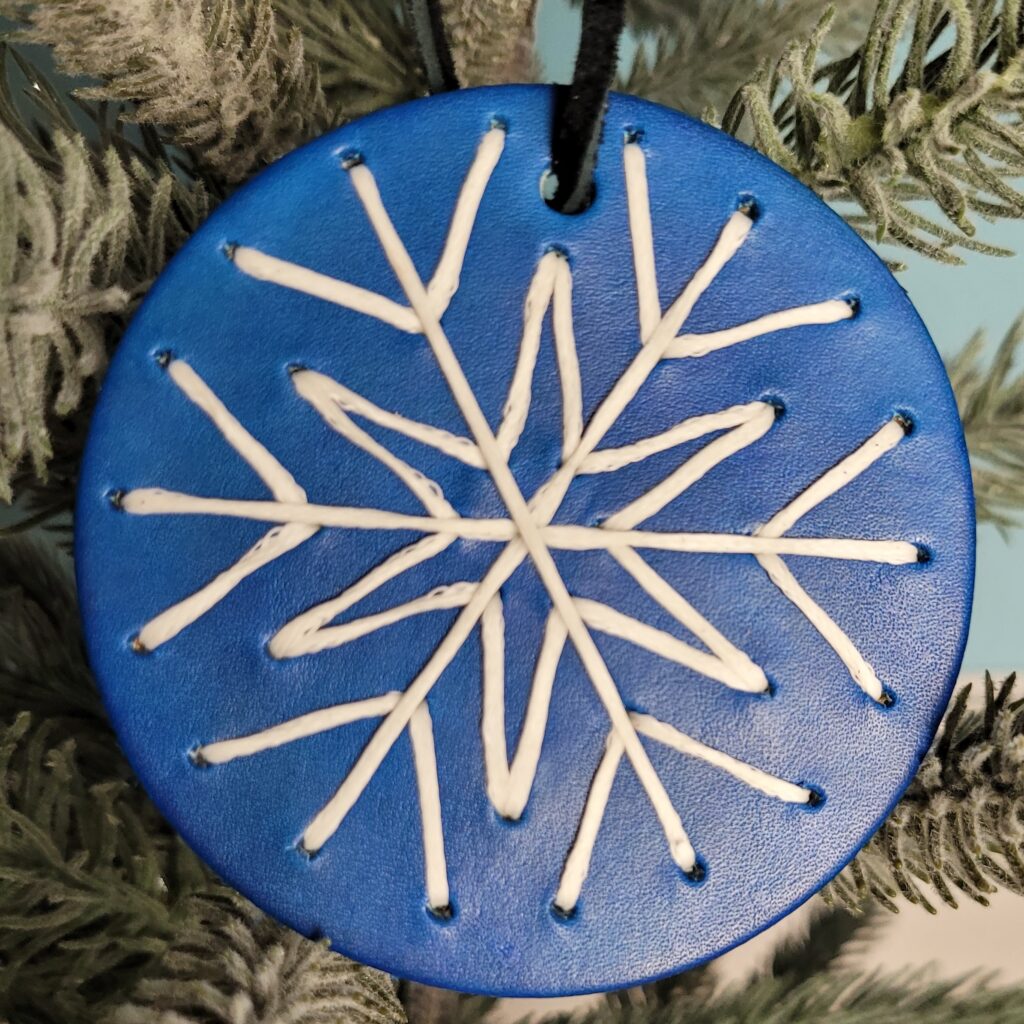Snowflake ornament. A round bright blue background with a intricate white snowflake stitched on front.