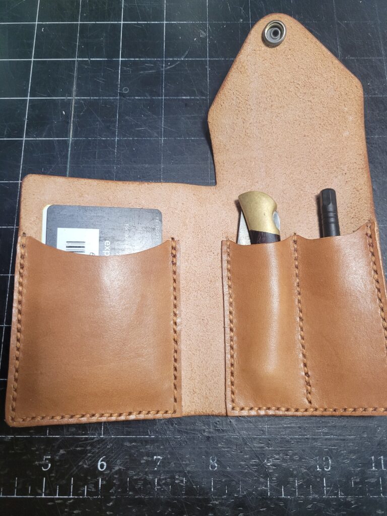 A natural leather colored wallet.  Folds open with small pockets containing card, knife, and other small tool